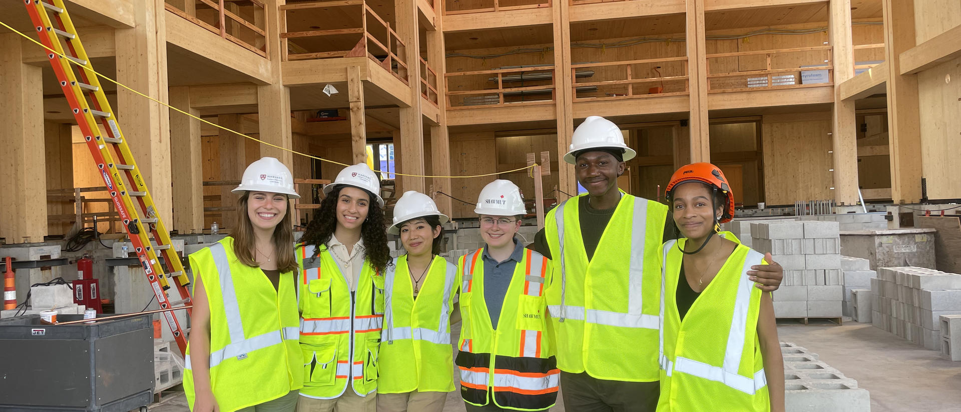 A group of students wearing safety vests and hard hats stand together at a construction site.