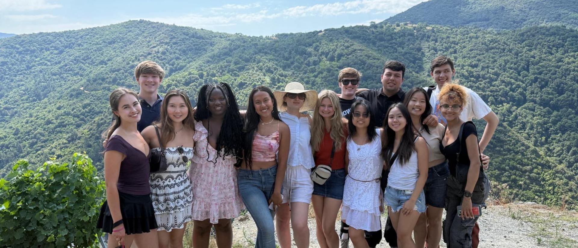 Group of students posing together outdoors with green hills and blue sky in the background.